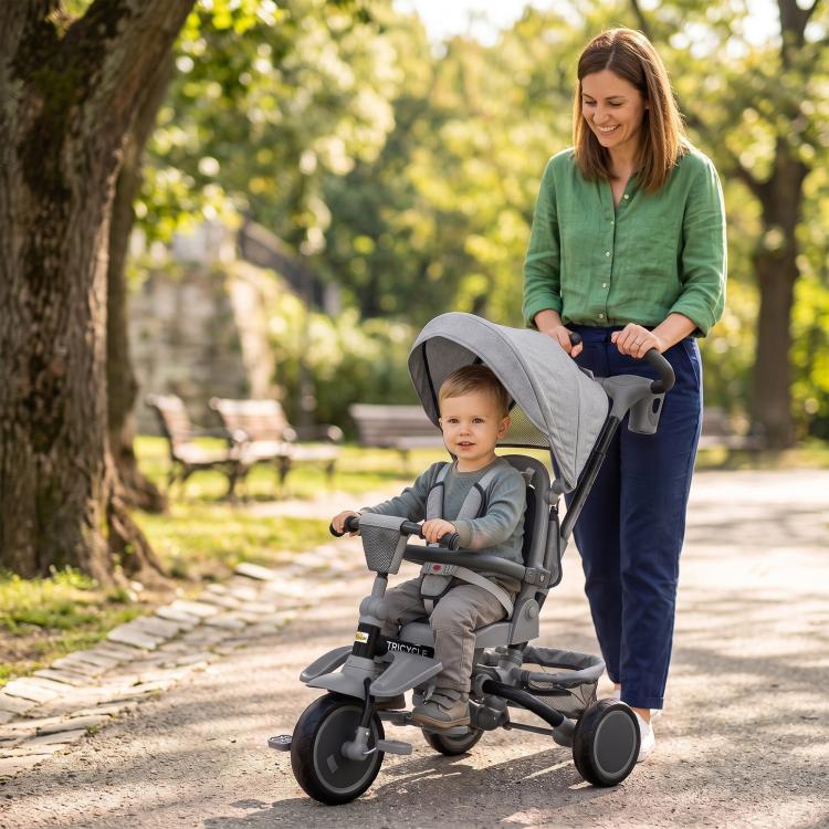 Gray kids tricycle stroller with canopy and handlebar, parked on a sidewalk