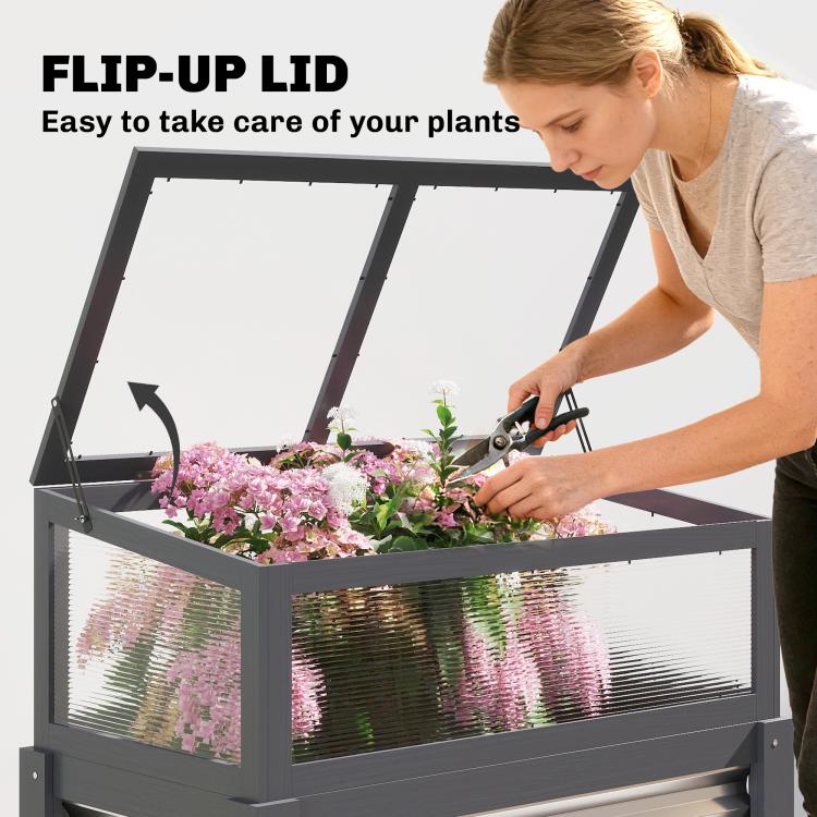 Gray flip-up mini greenhouse lid opened over planted flowers in raised planter box