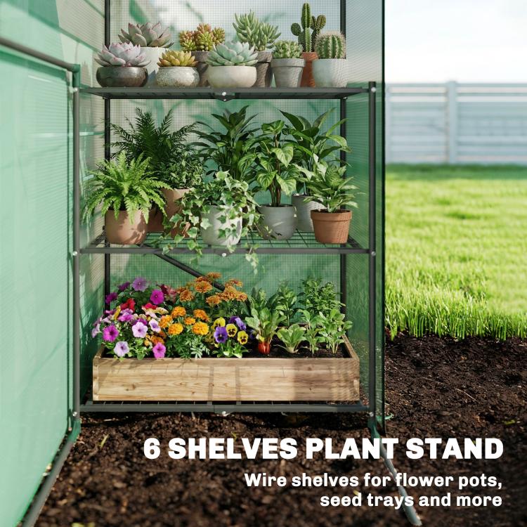 Green portable greenhouse with wire shelves holding potted plants and flowers
