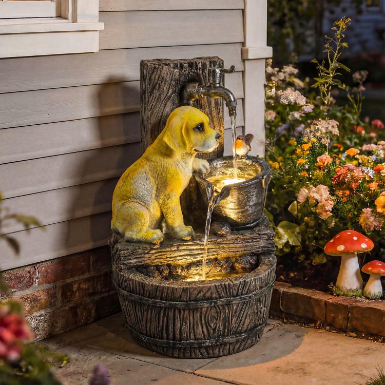 Dog statue drinking pose next to a flowing three-tier fountain with warm light.