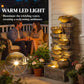 Warm-lit tiered jug fountain with cascading water and rustic stone texture