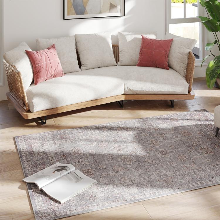 Grey and brown traditional floral area rug beneath a couch and decor on wood flooring