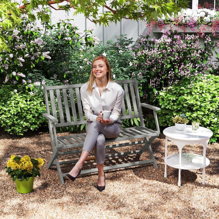 Gray 2-seat outdoor bench with slatted backrest and arms beside flowers