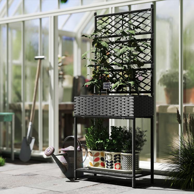 Black outdoor wicker planter with trellis, green plants and lower shelf in a greenhouse setting