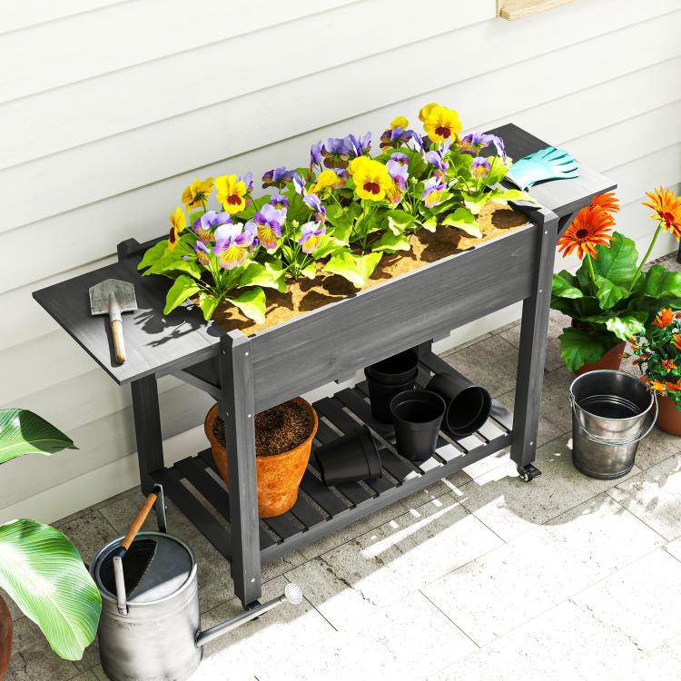 Gray raised wooden planter box with lockable wheels, side shelf, and planted flowers