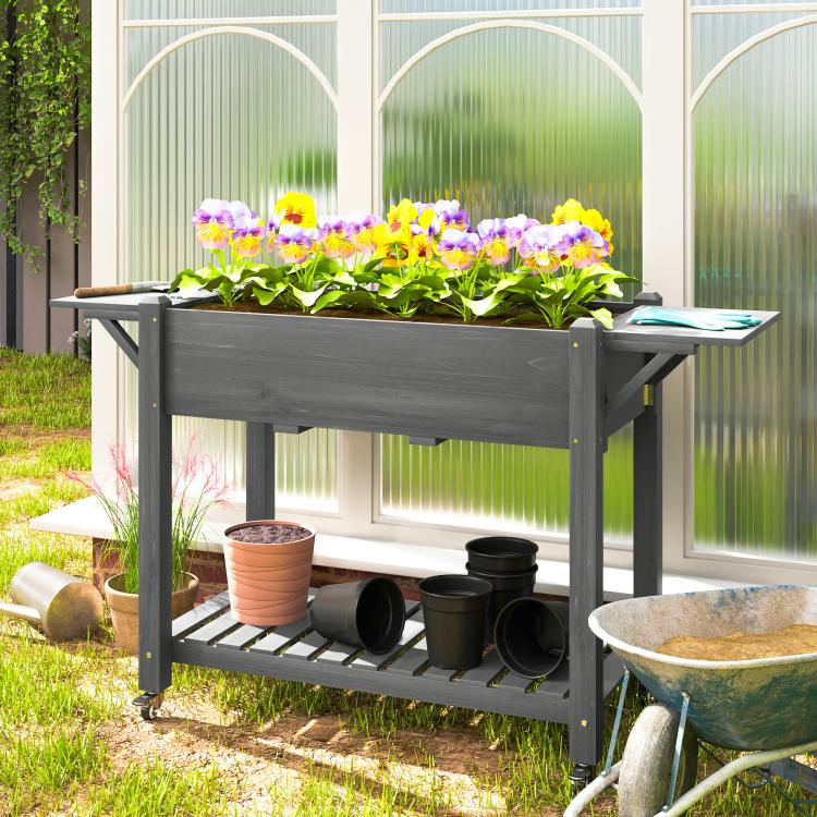Gray raised planter box with flowering plants and bottom shelf holding nursery pots