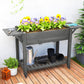 Gray wooden raised planter box with flowers, side table, watering can, and bottom shelf
