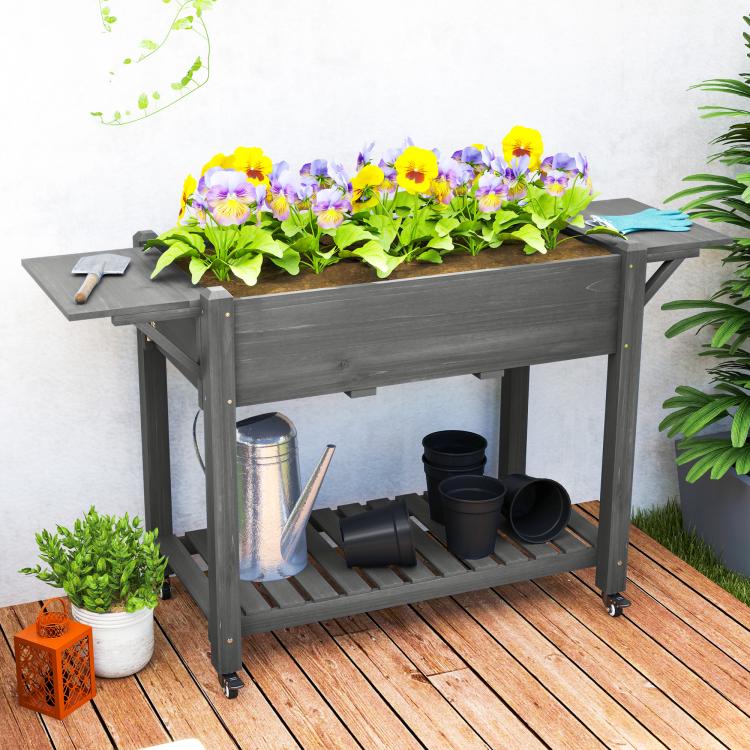 Gray wooden raised planter box with flowers, side table, watering can, and bottom shelf