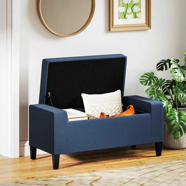 Dark blue upholstered storage ottoman bench with open lid holding pillows and items