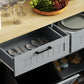 Gray kitchen cabinet with open drawers and tilt-out hidden trash bin, interior shelves visible