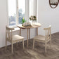Round drop-leaf dining table with light oak tabletop and four wooden legs beside chairs