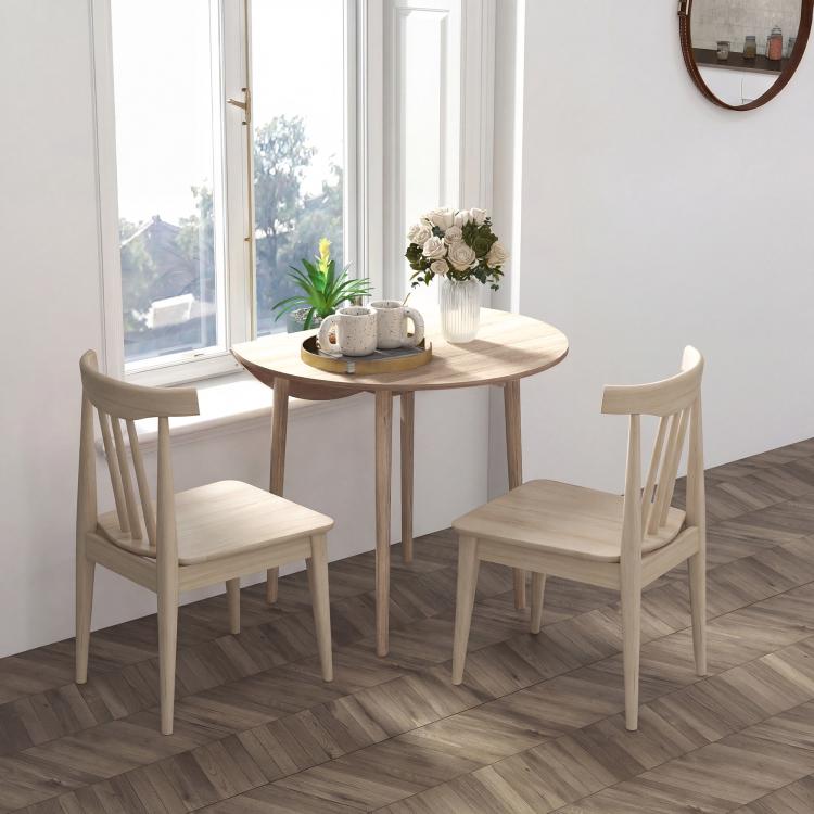 Round drop-leaf dining table with light oak tabletop and four wooden legs beside chairs