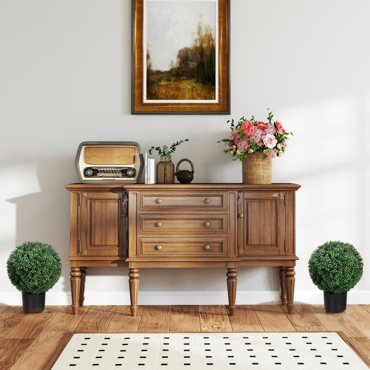 Two artificial ball topiary trees in matte black pots beside a wooden sideboard.