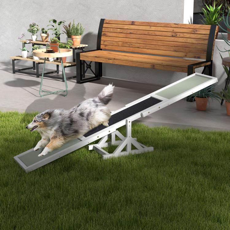 White wooden dog agility seesaw with green ramps and black center strip, dog crossing