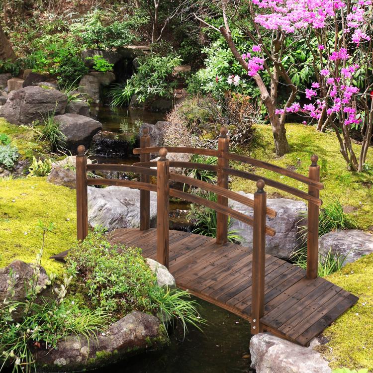 Wooden garden bridge with side railings and arched posts beside a pond