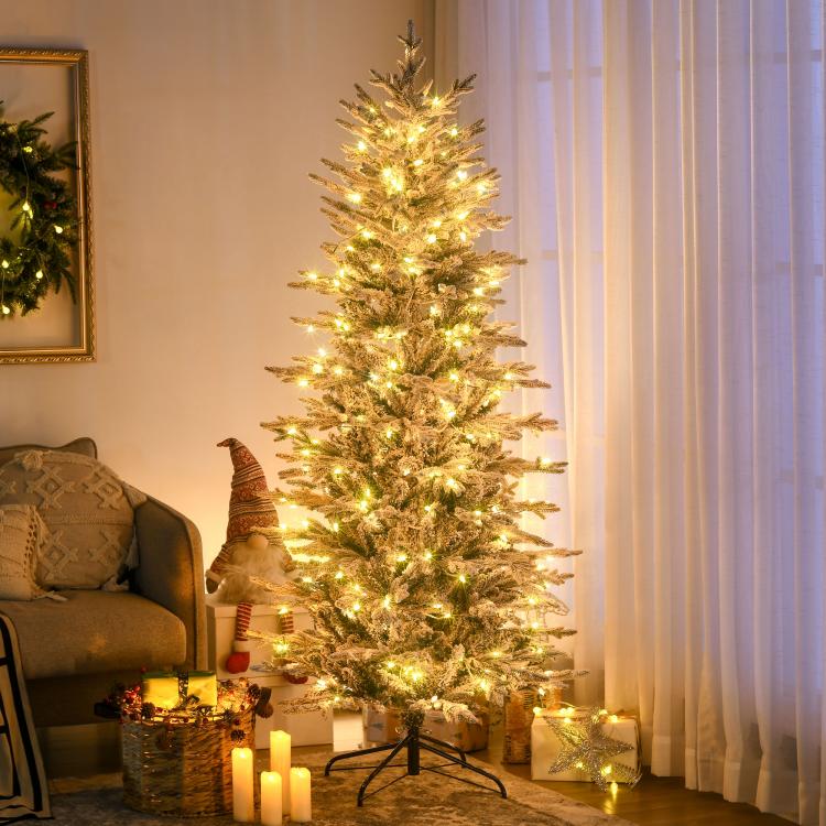 Snow-frosted artificial Christmas tree with warm clear lights on black tripod stand