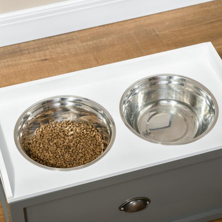 Two stainless steel pet bowls on gray elevated feeding station with kibble