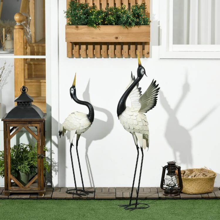 Two standing metal heron statues with black heads and white feathered bodies