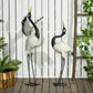 Two metal heron sculptures with black heads, white wings, and slender wire legs