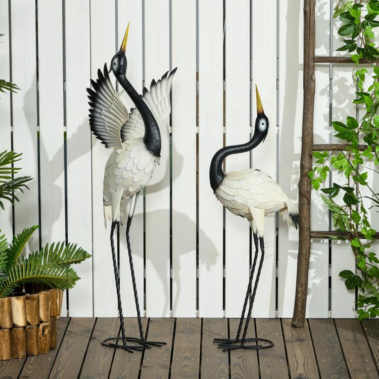 Two metal heron sculptures with black heads, white wings, and slender wire legs