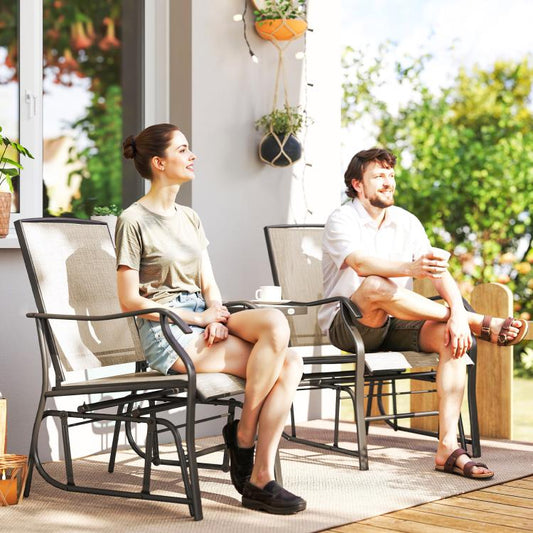 Outdoor rocking glider chairs with light beige sling seats and dark metal frames, table between