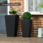 Two black tall square planters with small potted greenery
