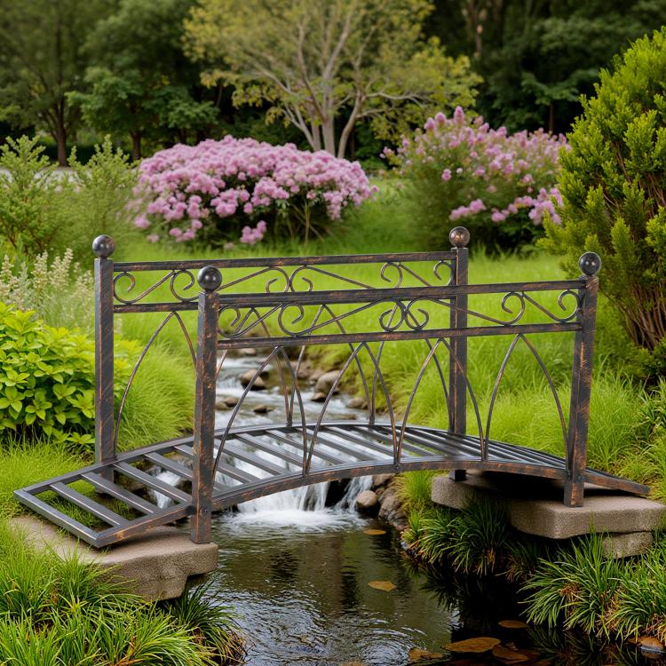 Bronze metal footbridge with arched railing and decorative scrollwork over a pond