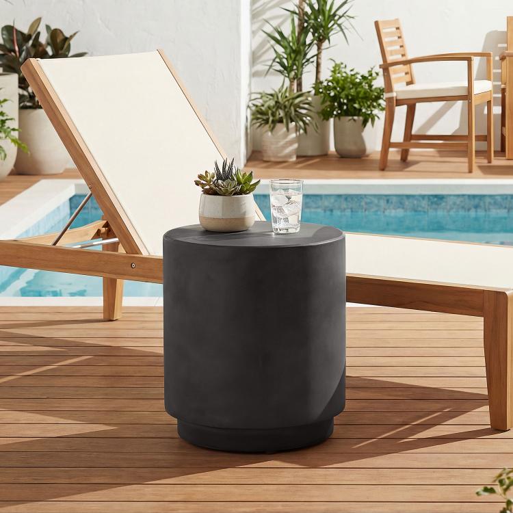 Round dark gray side table with concrete-look finish next to pool deck