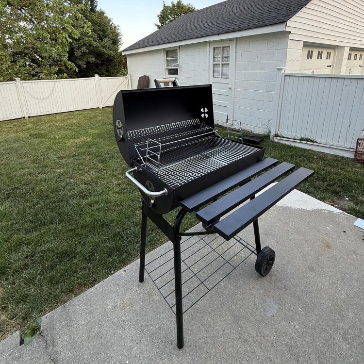 Charcoal barbecue grill with open lid, wire cooking grate, side shelves, and wheels