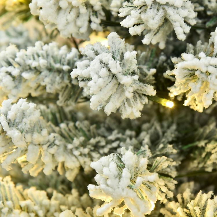 Snow-flocked artificial Christmas tree close-up with glowing warm LED lights