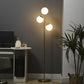 Gold standing floor lamp with three lit white globe glass shades on a slim pole