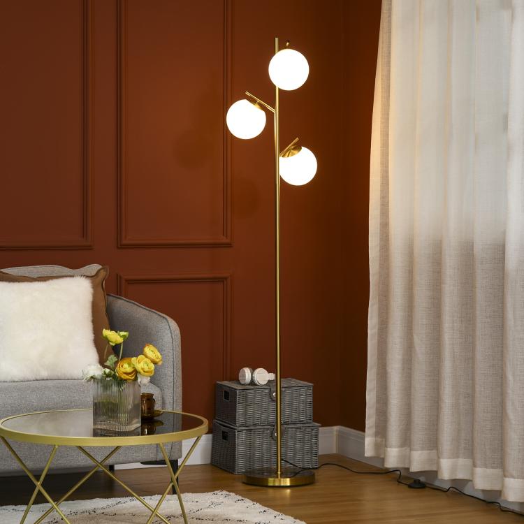 Gold standing floor lamp with three lit white globe glass shades on slim branches