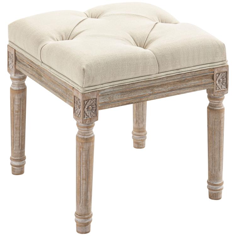Beige ottoman bench with tufted seat, rounded edges, and carved wooden frame