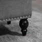 Gray upholstered storage ottoman with button-tufted side and black turned legs