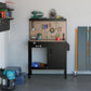 Black tool workbench with tan pegboard backing and storage cabinet with open lower shelf