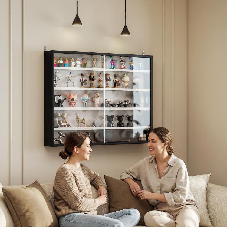 Black wall-mounted display cabinet with glass doors above a sofa, showing small figurines inside.
