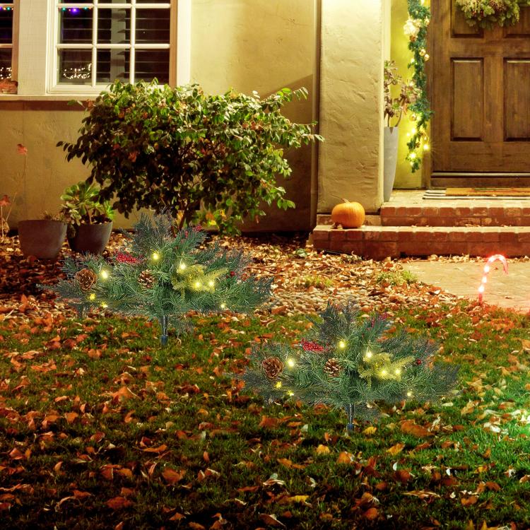 Pre-lit artificial Christmas tree with warm white lights and red berry details in front yard