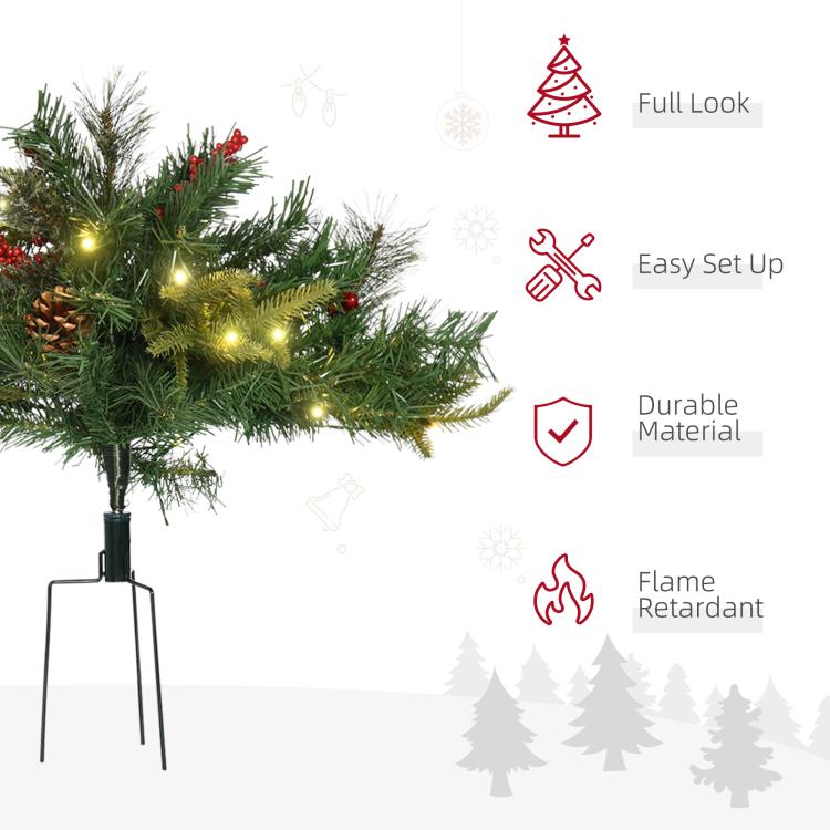 Pre-lit artificial Christmas tree with warm white lights and red berries, standing on metal legs