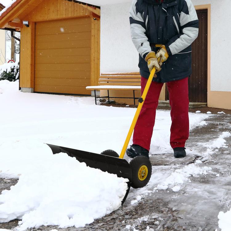 Yellow rolling snow pusher shovel with black angled blade on packed snow