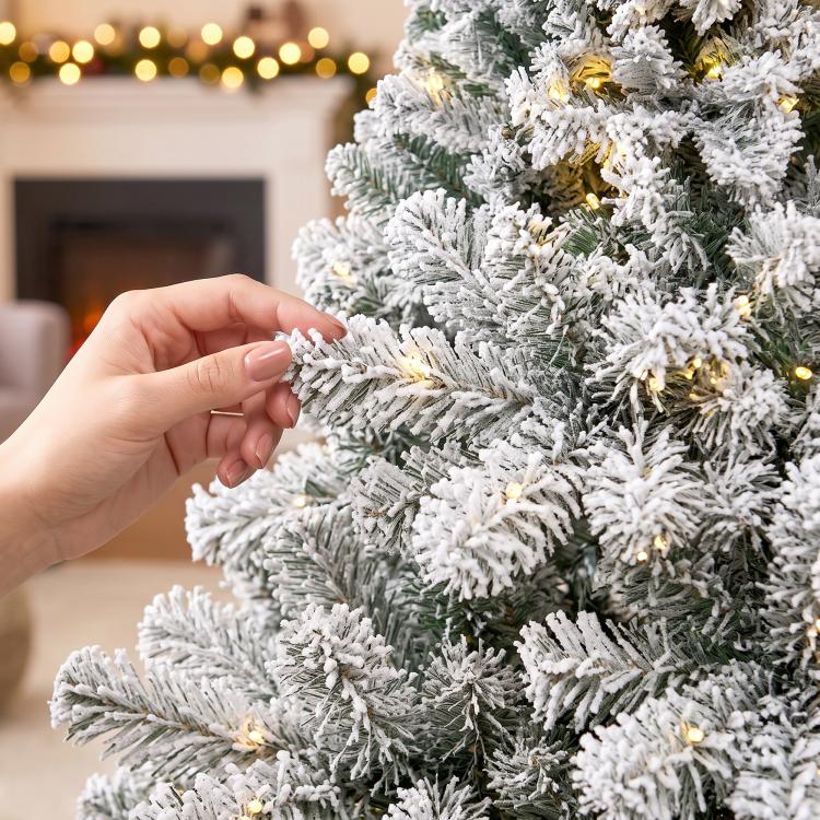 Flocked prelit Christmas tree branch tip with warm lights, close-up of hand adjusting