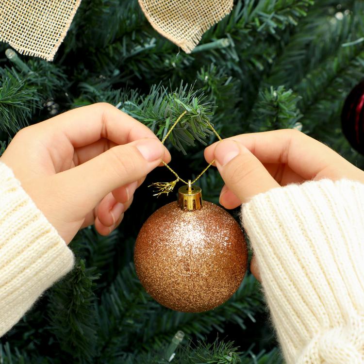 Artificial Christmas tree branch with hands hanging a gold ornament