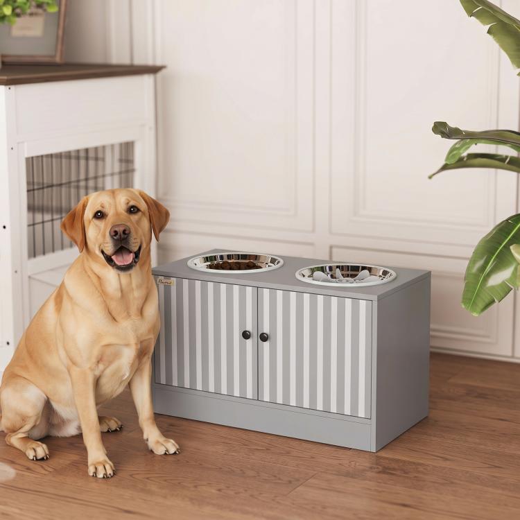 Tan dog sitting beside gray elevated feeding station with two stainless steel bowls