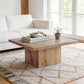 Light brown square center table with thick legs in a living room setting