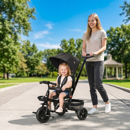 Black kids tricycle with canopy and parent handle while in use on a walkway