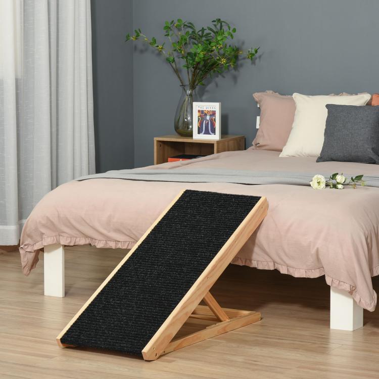 Pet ramp with black non-slip surface and light pine frame, placed for bed access