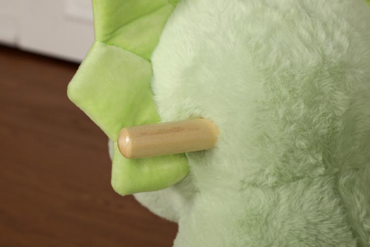 Green plush dinosaur rocking horse with wooden handle on its side