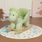 Green plush dinosaur rocking horse with wooden rockers, three-quarter view on play mat