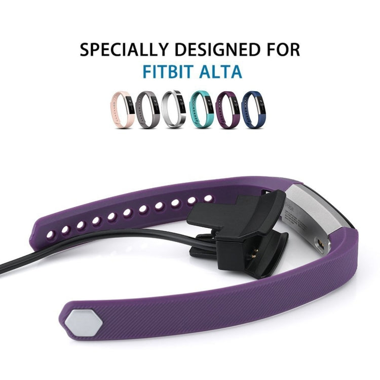 Fitbit Alta watch with purple band connected to black charging clip and cable