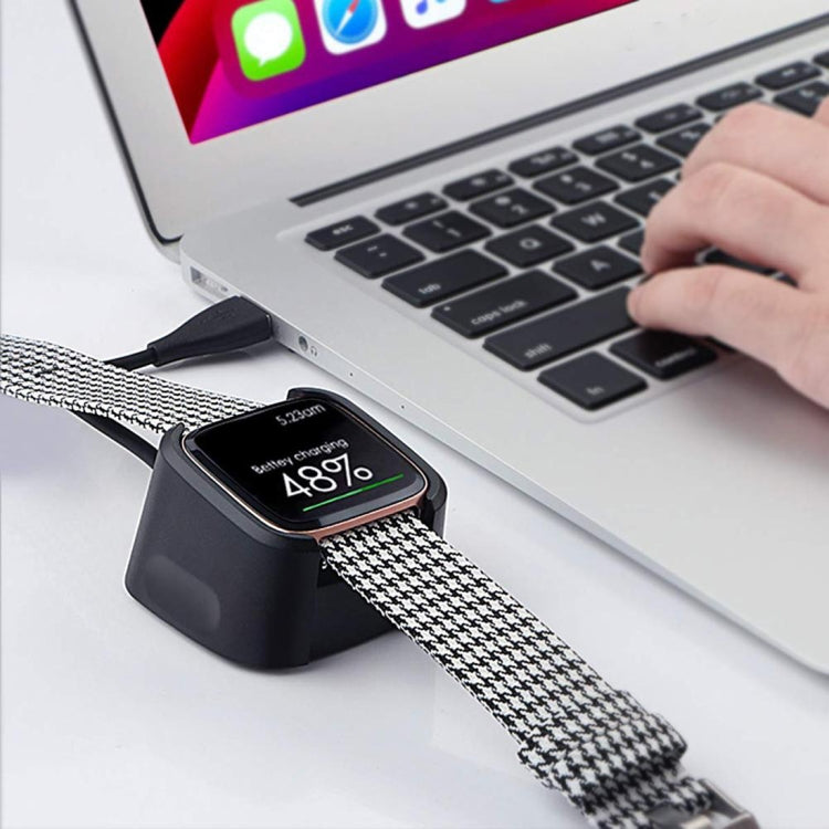 Black charging dock stand charging a smartwatch with braided strap by laptop