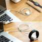 White charging puck with cable coiled near a smartwatch on a wooden desk.